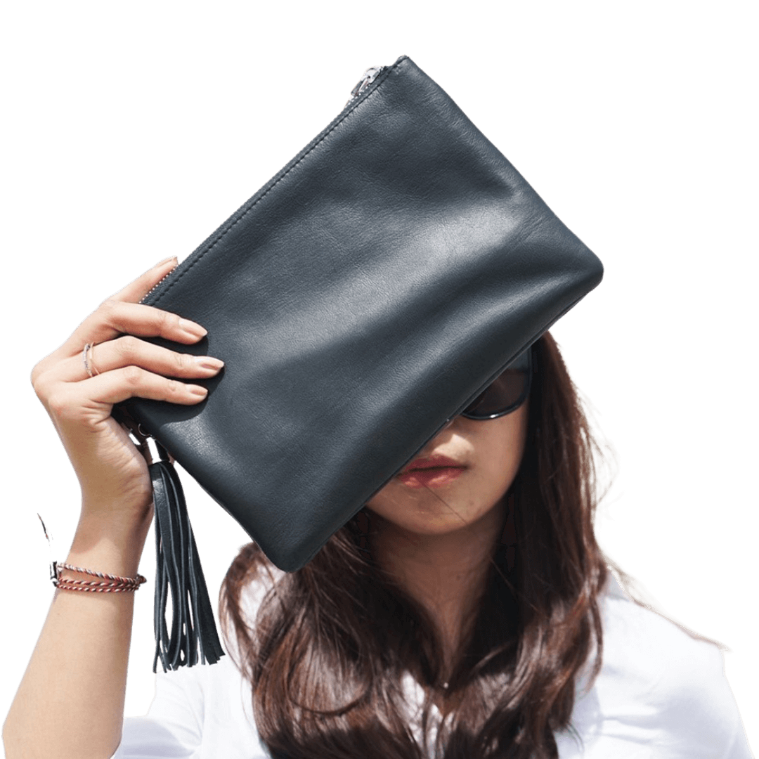 A model looking ahead, holding a clutch. Clutch made of sheep leather measuring 24 x 16 cm. The black color give you a style to make it formal or informal style.