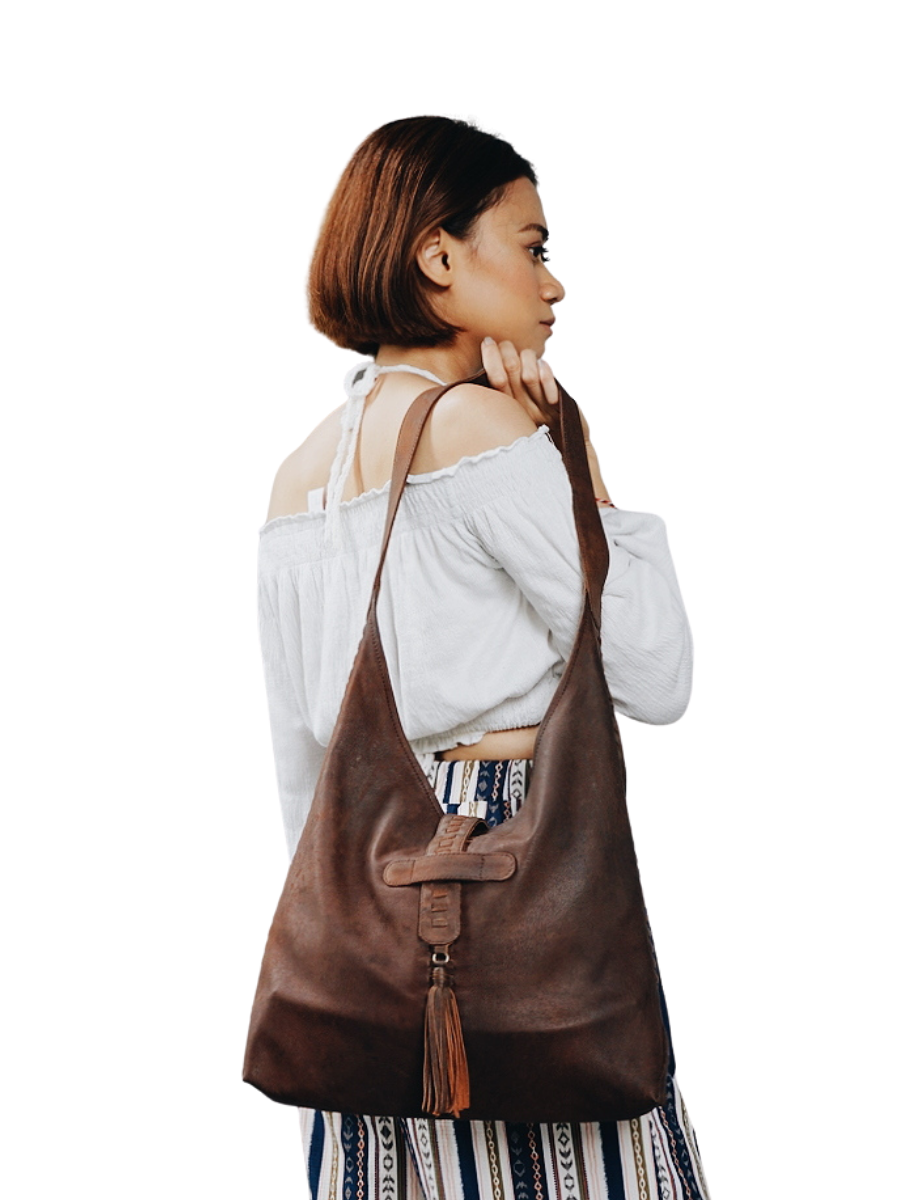 A picture shows a model in white blouse hold a bag in her shoulder. It is Ella Hobo Bag from Seminyak Leather Bali.