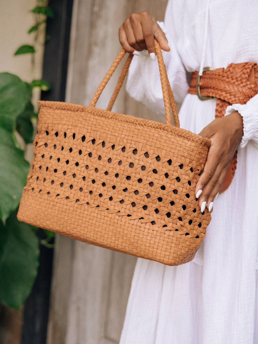 A woman hold tan medium-sized rectangle handbag made of hand-weaved leather with braided handle and chick-eye weave on the body by Seminyak Leather Bali. A blend of modern elegance and artisanal charm, crafted with meticulous attention to detail.