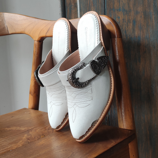 White pointy toe mules by Seminyak Leather Bali with western-style stitching on vamp and carved metal toe cap and carved buckle. 5 cm wooden Cuban heel in a natural finish. A blend of Western charm and contemporary elegance, all made of leather.