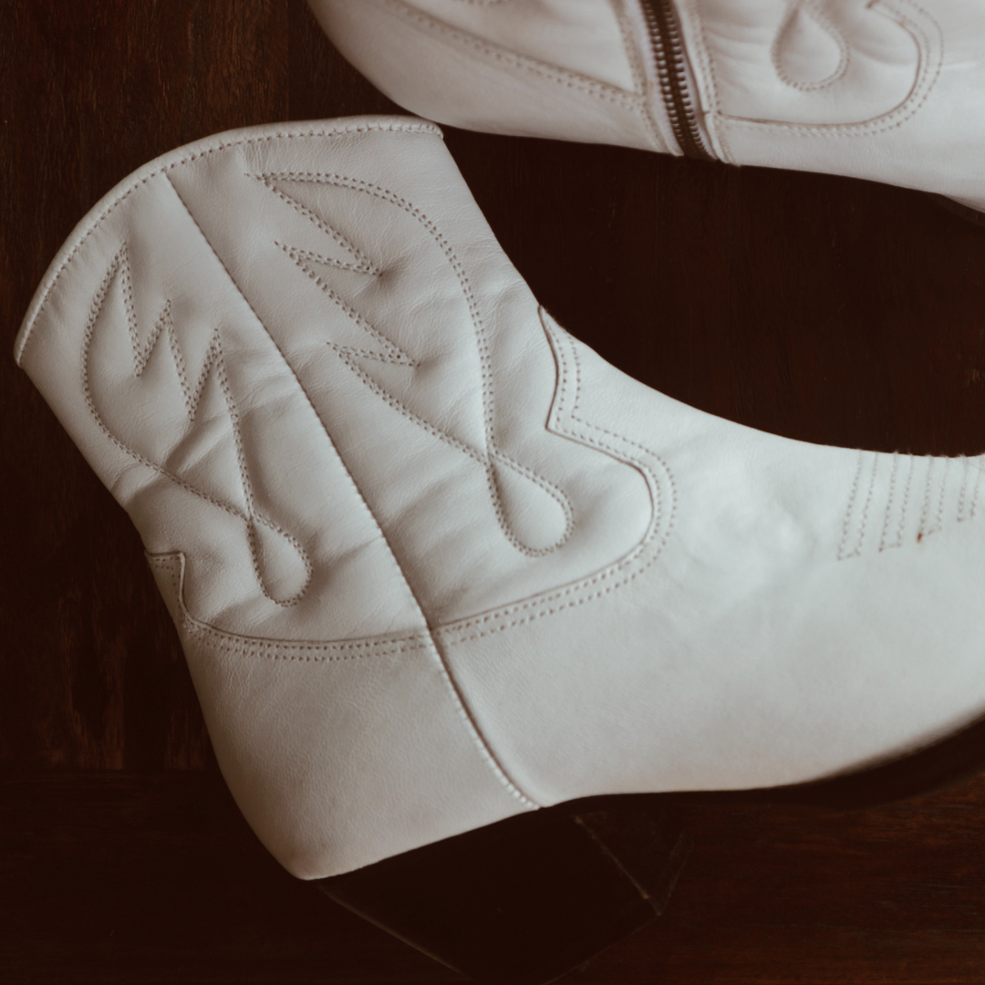 Ankle boots with handstitched detailing, featuring zipper closure and carved metal accents on the toe cap and heel. 5 cm wooden heel in a classic black finish. Stylish footwear inspired by cowboy/ western ankle boots for a touch of rustic charm and modern allure.