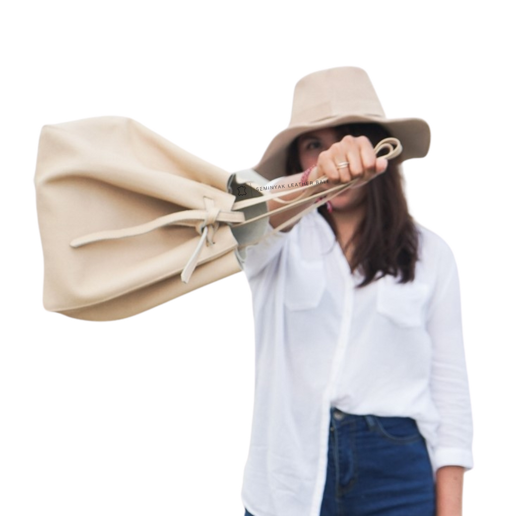 A person holding a beige pebble grain cow leather tote bag with a drawstring style ribbon tape designs by Seminyak Leather Bali.