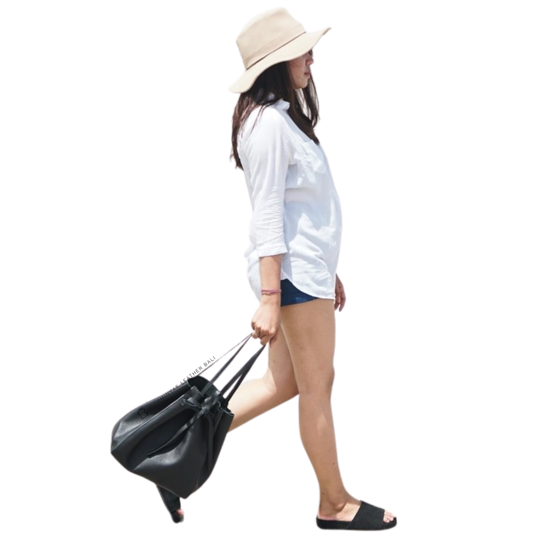 A person holding a black pebble grain cow leather tote bag with a drawstring style ribbon tape designs by Seminyak Leather Bali.