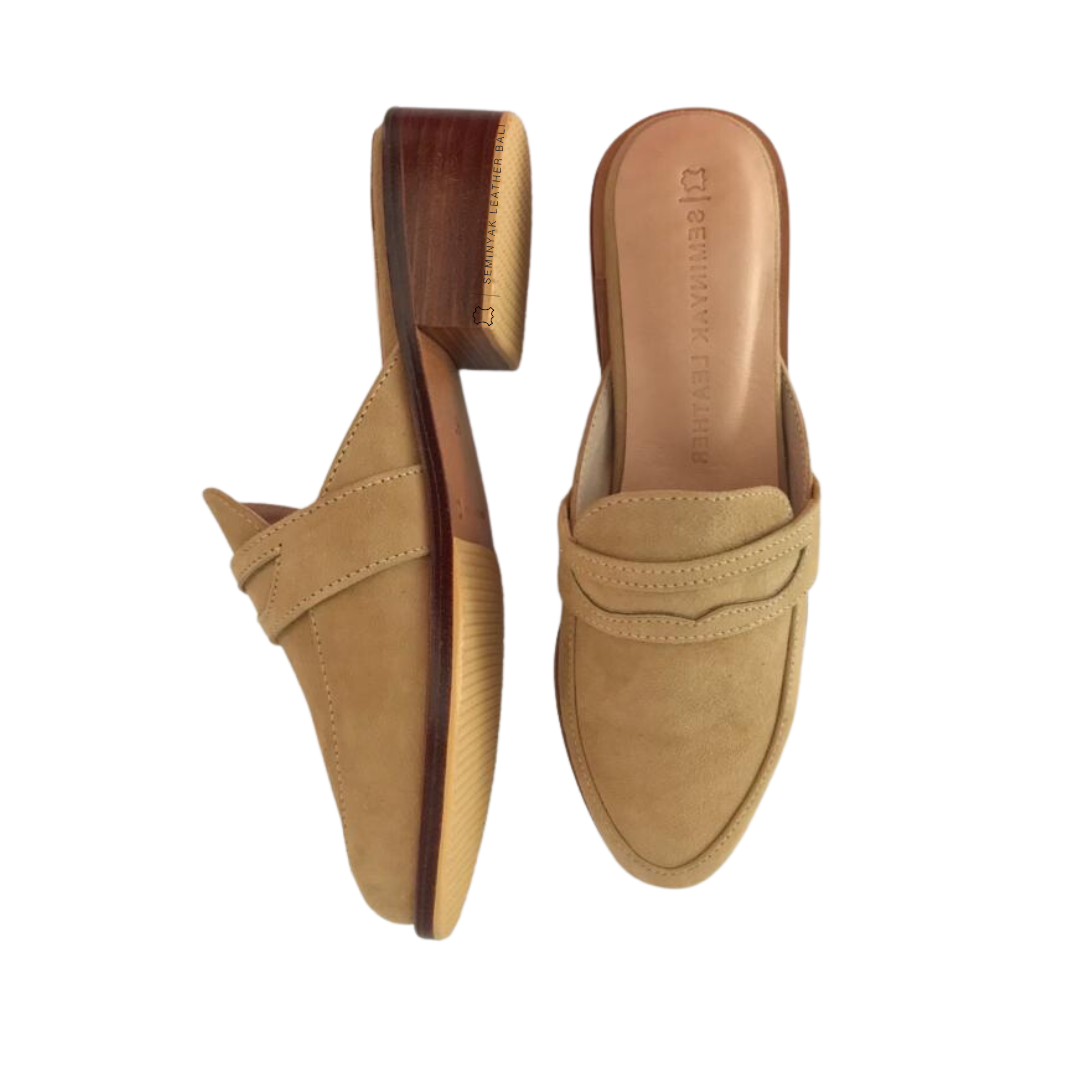 A pair of beige suede loafer mules with wooden heels, displayed against a white background designs by Seminyak Leather Bali