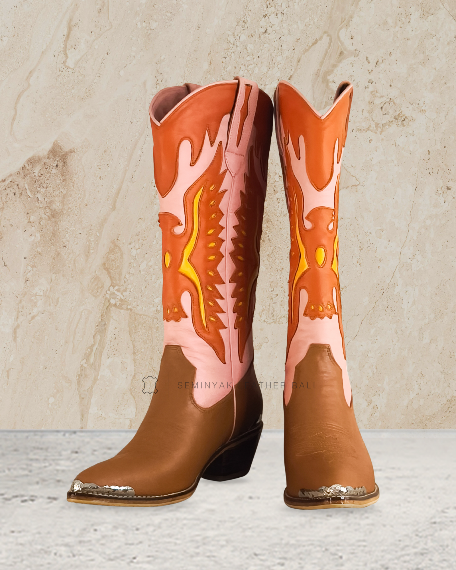 pink orange knee high cowboy boot with decorative patterns designs by Seminyak Leather Bali on a textured beige background