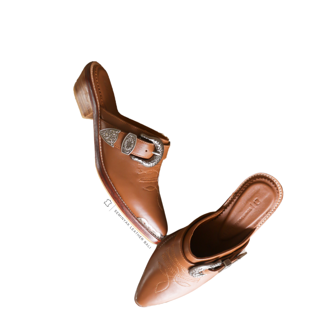 Tan pointy toe mules by Seminyak Leather Bali with western-style stitching on vamp and carved metal toe cap. 5 cm wooden Cuban heel in a natural finish. A blend of Western charm and contemporary elegance, all made of leather.