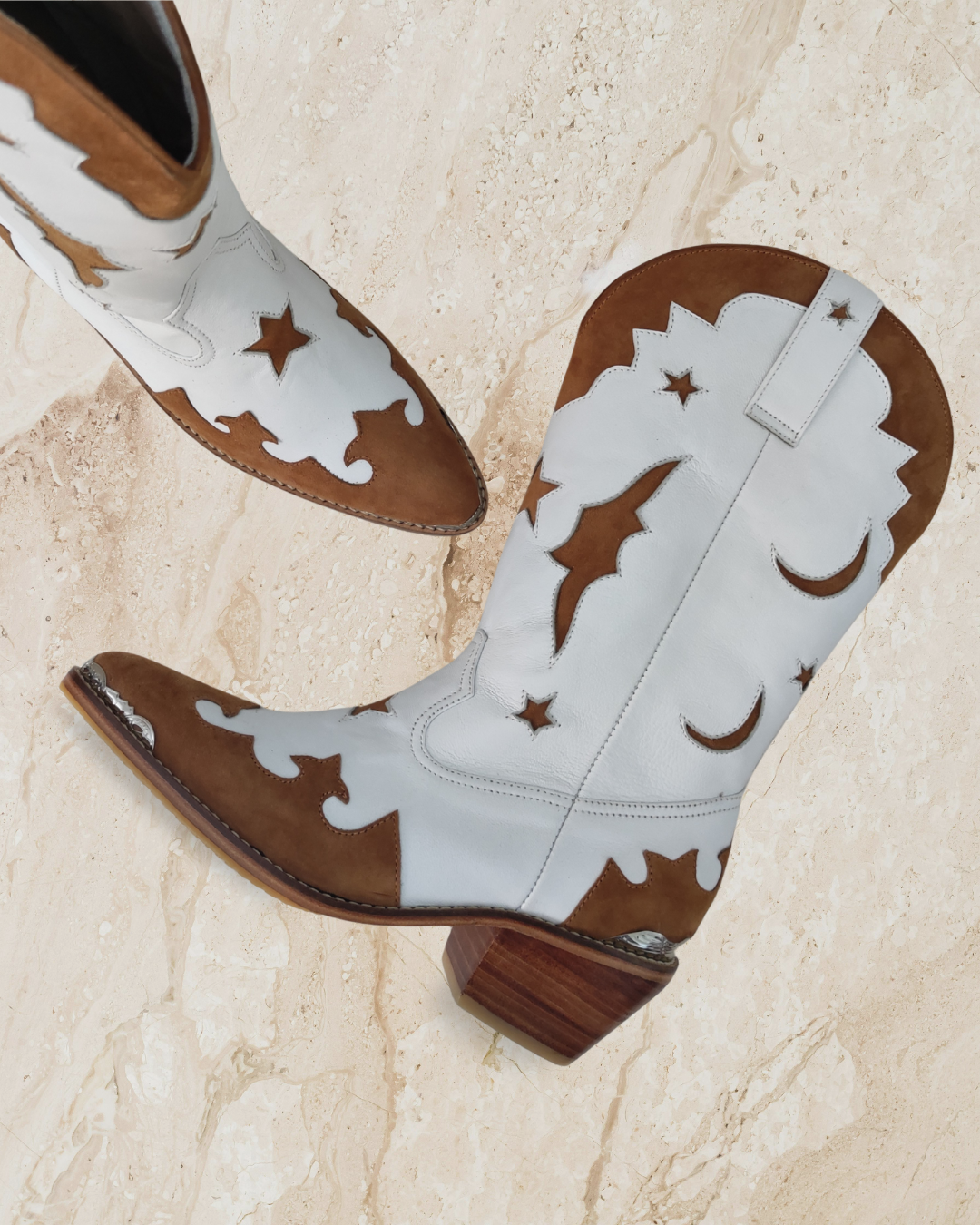 White cowboy boot with brown accents designs by Seminyak Leather Bali on a textured beige background