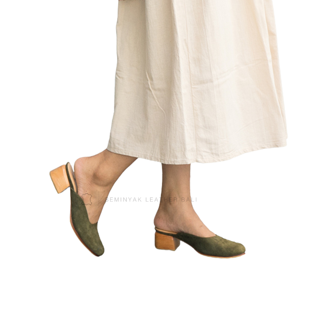 A person wearing green suede mule heels with wooden block heels, paired with a beige skirt designs by Seminyak Leather Bali