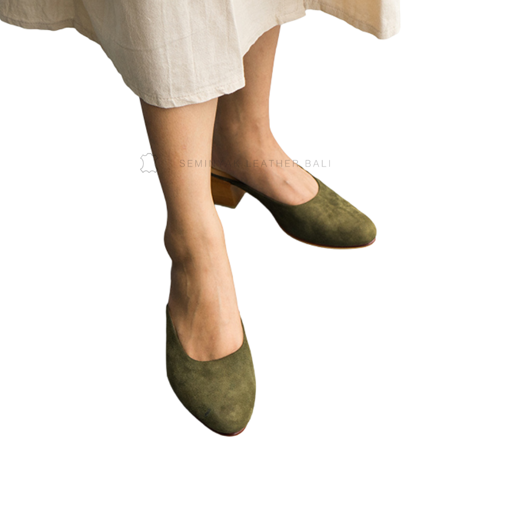 A person wearing green suede mule heels with wooden block heels, paired with a beige skirt designs by Seminyak Leather Bali