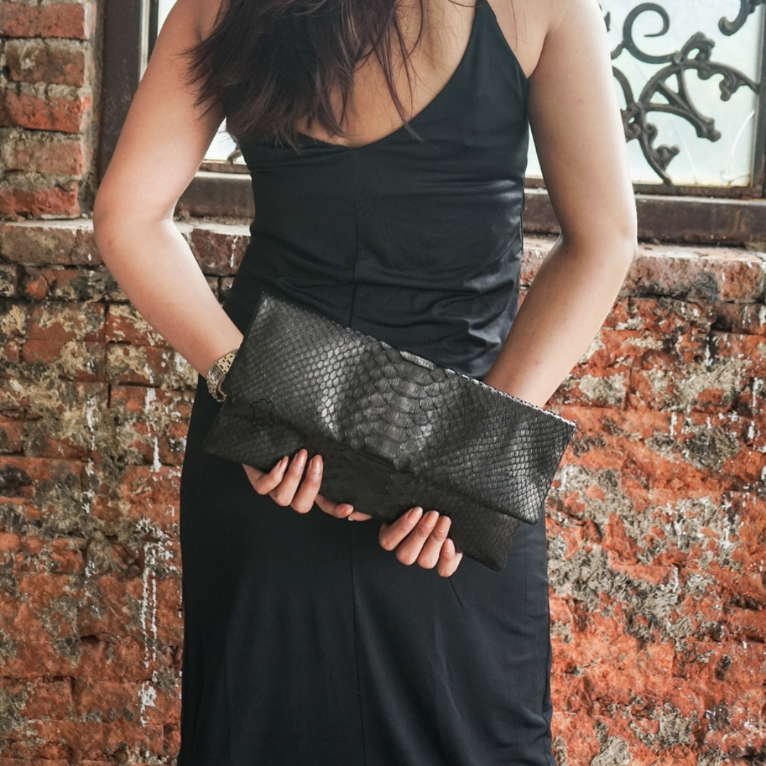 A person holding a black python folded clutch with a textured exterior designs by Seminyak Leather Bali 