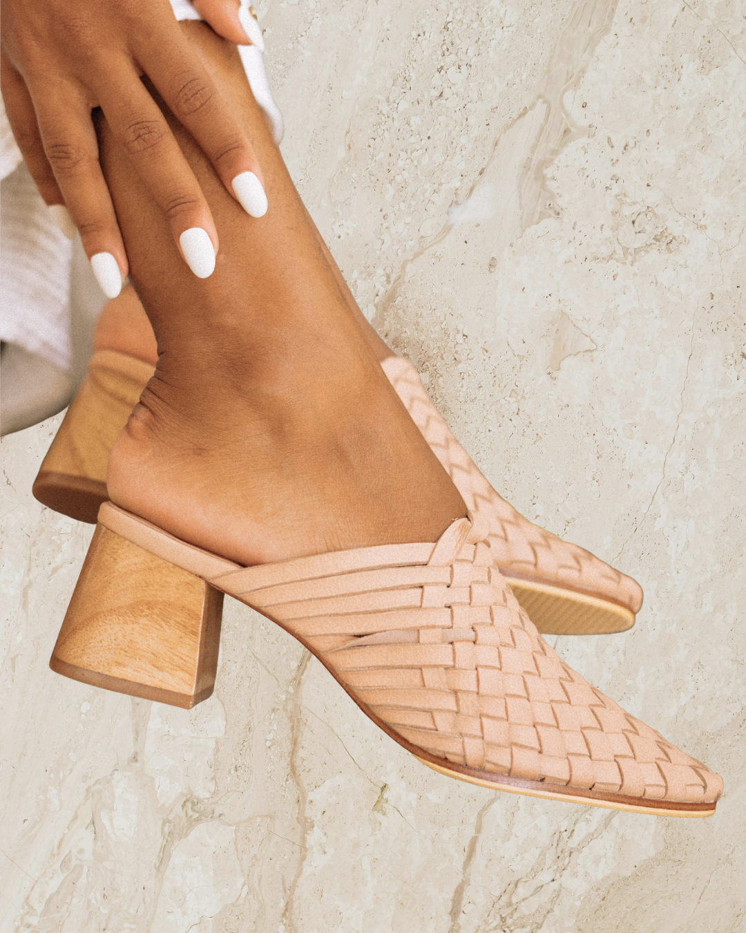 Pair of blush woven mule heels designs by Seminyak Leather Bali on a beige marble surface