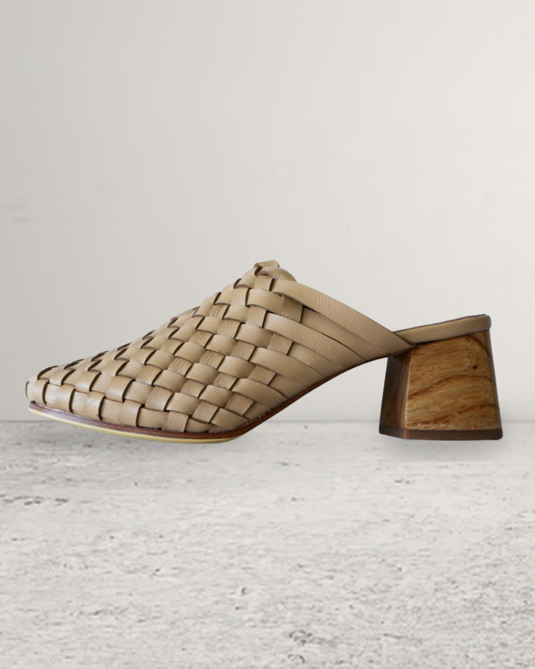 Pair of nude beige woven mule heels designs by Seminyak Leather Bali on a beige marble surface
