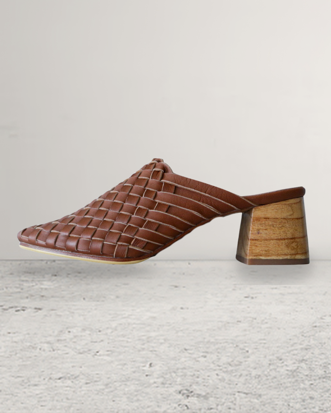 Pair of summer tan woven mule heels designs by Seminyak Leather Bali on a beige marble surface