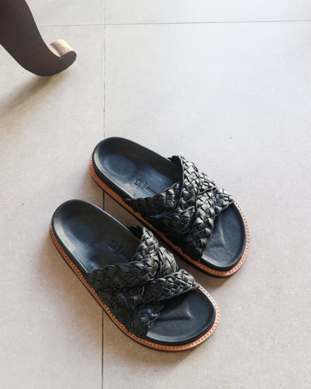 Pair of black woven sandals on a light tiled floor