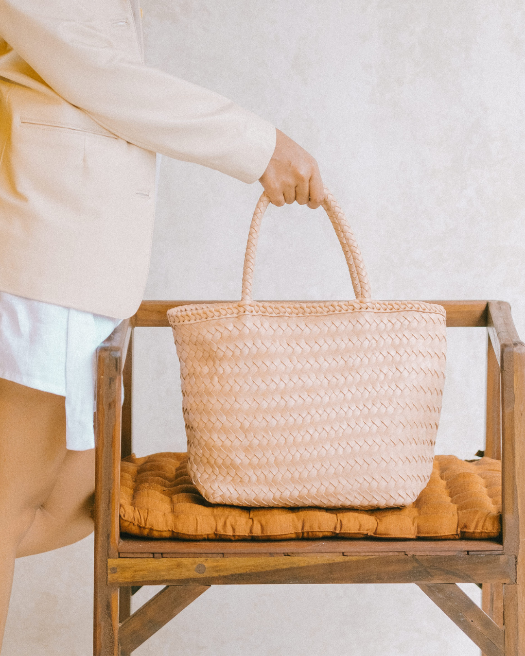 Person holding a blush woven basket on a wooden chair with a white background designs by Seminyak Leather Bali