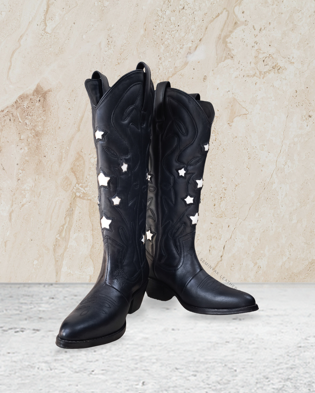Black cowboy boots with star patterns by Seminyak Leather Bali on a light stone background