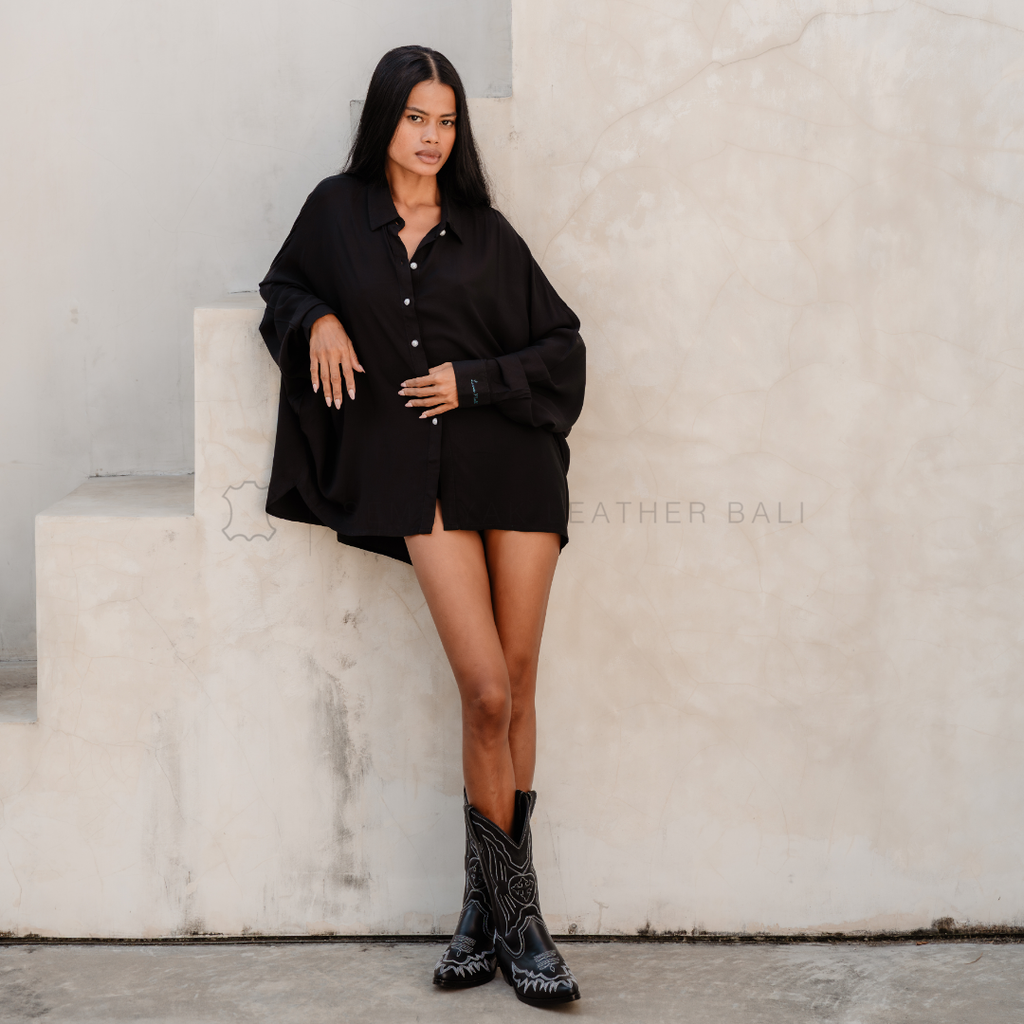 Woman in a black outfit wearing black cowboy western leather boots standing on stone steps with a neutral background