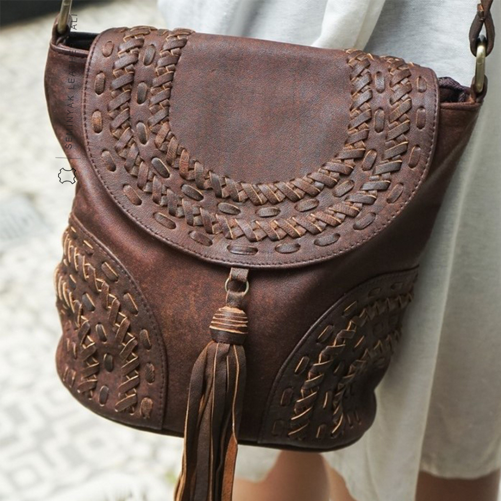 A person wearing a white dress is carrying a brown crossbody bag with woven details and a tassel designs by Seminyak Leather Bali