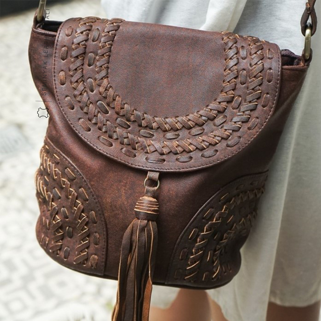 A person wearing a white dress is carrying a brown crossbody bag with woven details and a tassel designs by Seminyak Leather Bali