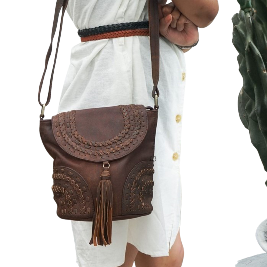 A person wearing a white dress is carrying a brown crossbody bag with woven details and a tassel designs by Seminyak Leather Bali