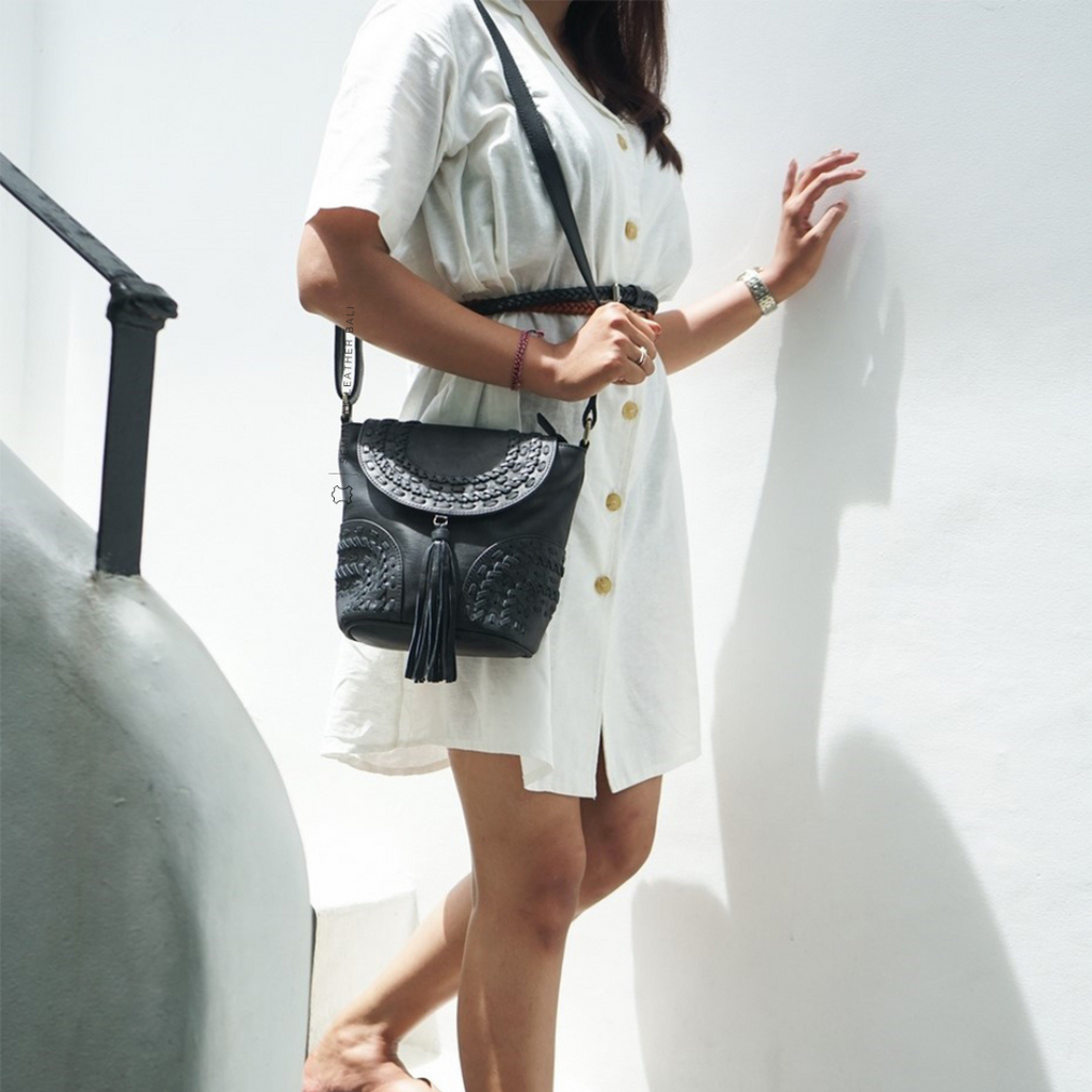 A person wearing a white dress is carrying a black crossbody bag with woven details and a tassel designs by Seminyak Leather Bali