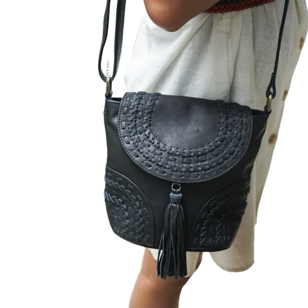 A person wearing a white dress is carrying a black crossbody bag with woven details and a tassel designs by Seminyak Leather Bali

