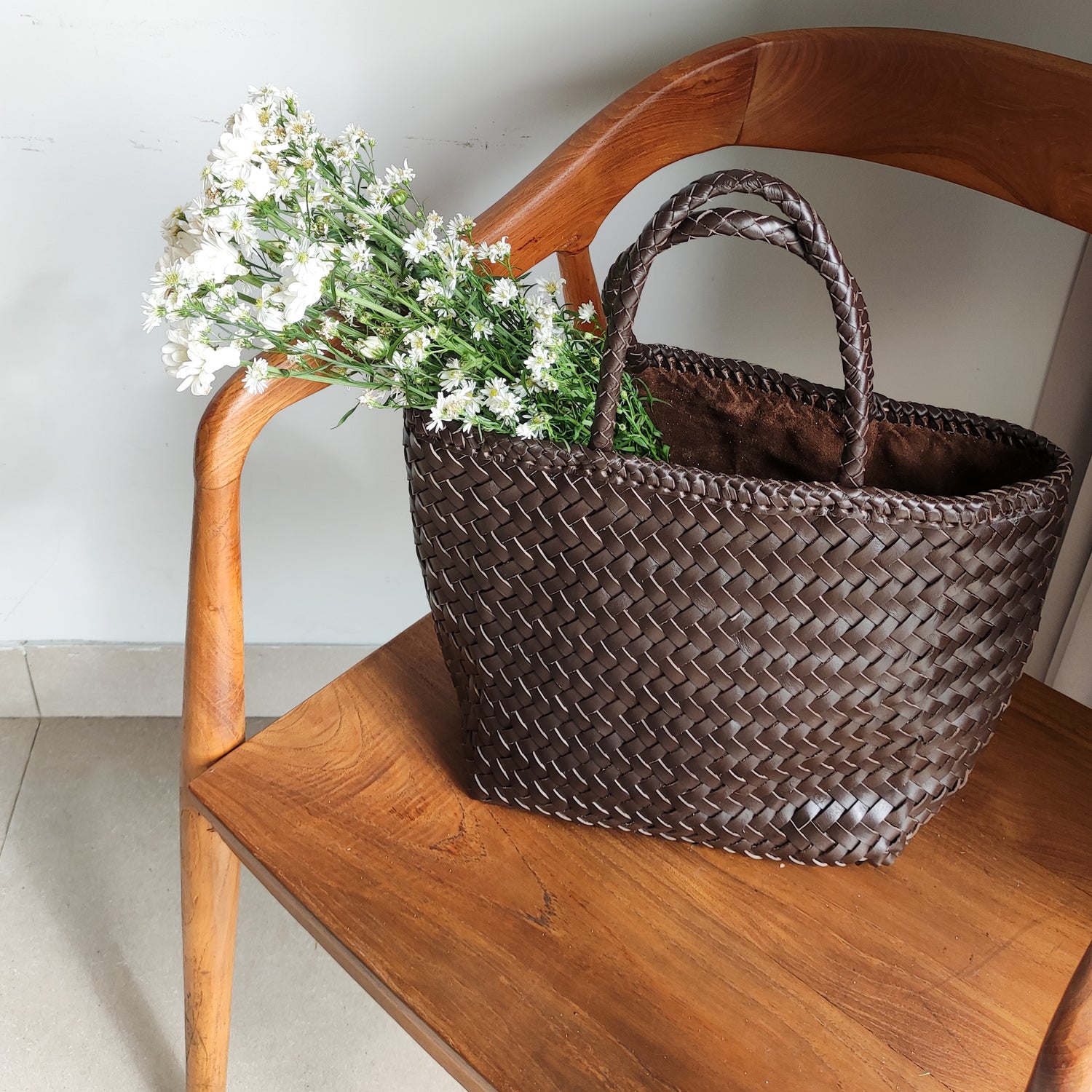 A woven bag placed on a wooden chair is the Cening Woven Bag from Seminyak Leather Bali. This dark tan colored bag is made of vegtanned leather which is shaped using a woven method to form a strong and beautiful bag.