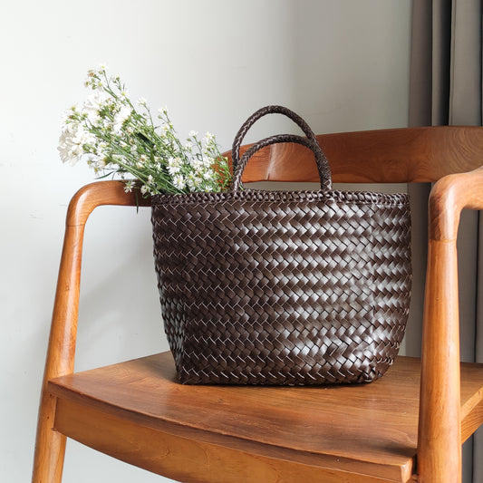 A woven bag placed on a wooden chair is the Cening Woven Bag from Seminyak Leather Bali. This dark tan colored bag is made of vegtanned leather which is shaped using a woven method to form a strong and beautiful bag.