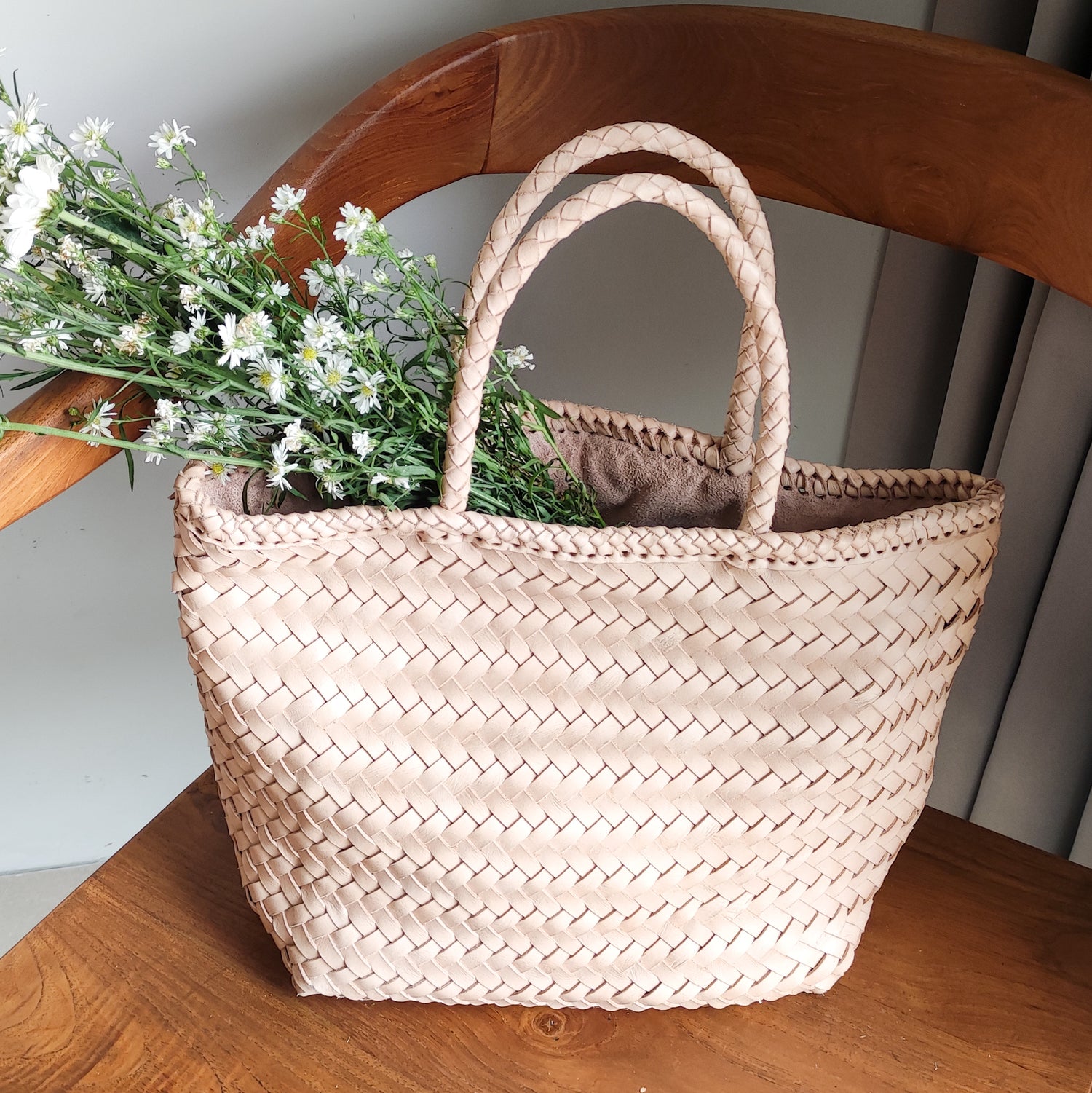 A woven bag placed on a wooden chair is the Cening Woven Bag from Seminyak Leather Bali. This natural blush colored bag is made of vegtanned leather which is shaped using a woven method to form a strong and beautiful bag.