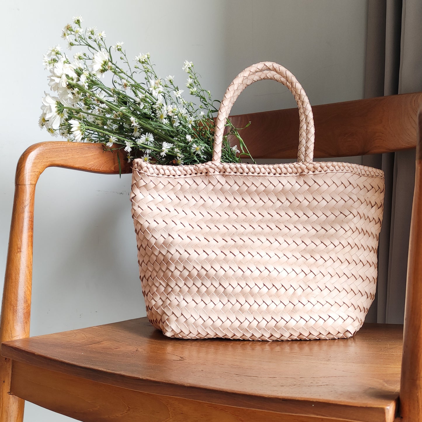 A woven bag placed on a wooden chair is the Cening Woven Bag from Seminyak Leather Bali. This natural blush colored bag is made of vegtanned leather which is shaped using a woven method to form a strong and beautiful bag.