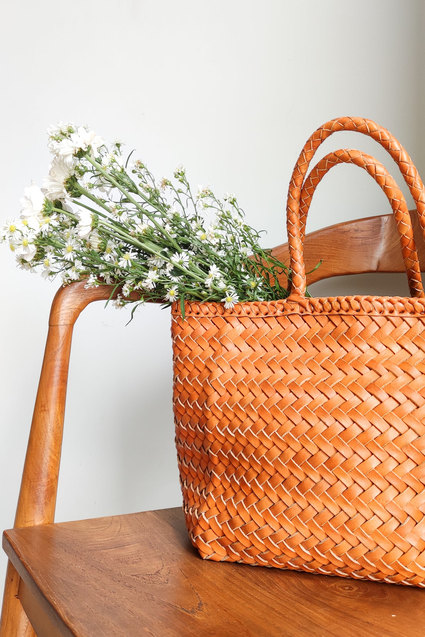 A woven bag placed on a wooden chair is the Cening Woven Bag from Seminyak Leather Bali. This honey tan colored bag is made of vegtanned leather which is shaped using a woven method to form a strong and beautiful bag.