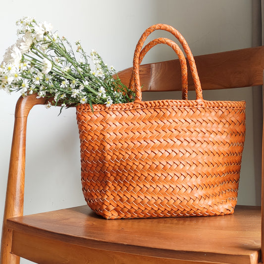 A woven bag placed on a wooden chair is the Cening Woven Bag from Seminyak Leather Bali. This honey tan colored bag is made of vegtanned leather which is shaped using a woven method to form a strong and beautiful bag.