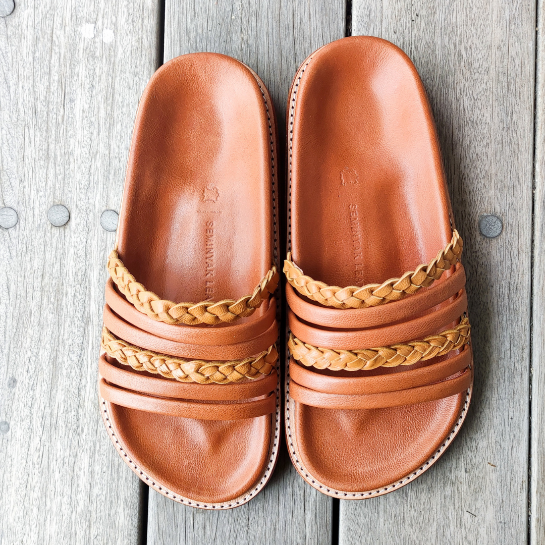 A slide put on the wood with a color combination of summer tan and honey tan. The braid detail on the strap doesn't make the sandals look boring. These are Dayana Slides from Seminyak Leather Bali.