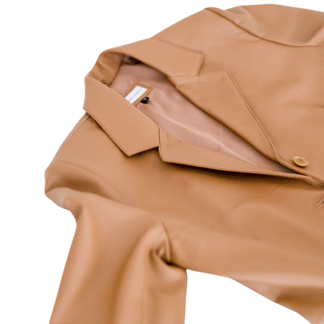 A close-up photo of the jacket spread out on the floor shows the details of the jacket on top. An Aubrey Oversize leather jacket from the Seminyak Leather Bali brand in an elegant Tan color