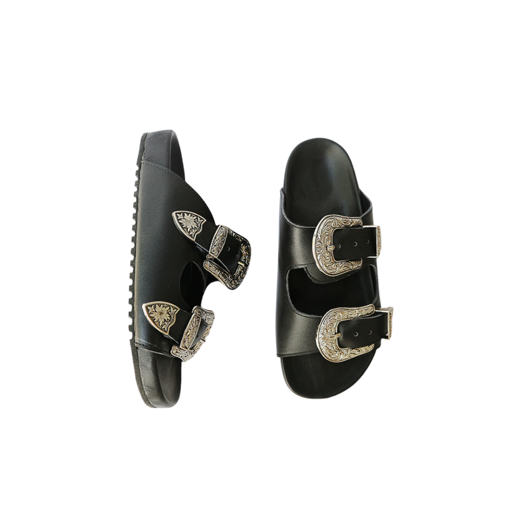 The image of a black sandal made of cowhide, designed with two straps and a carved buckle decoration is the Becky Slides Sandal from Seminyak Leather Bali