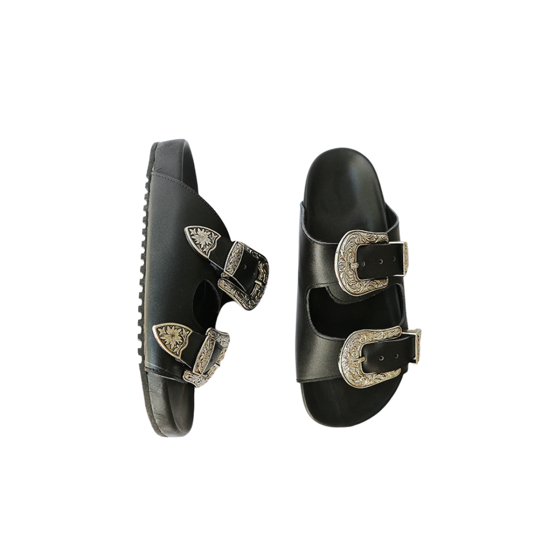 The image of a black sandal made of cowhide, designed with two straps and a carved buckle decoration is the Becky Slides Sandal from Seminyak Leather Bali