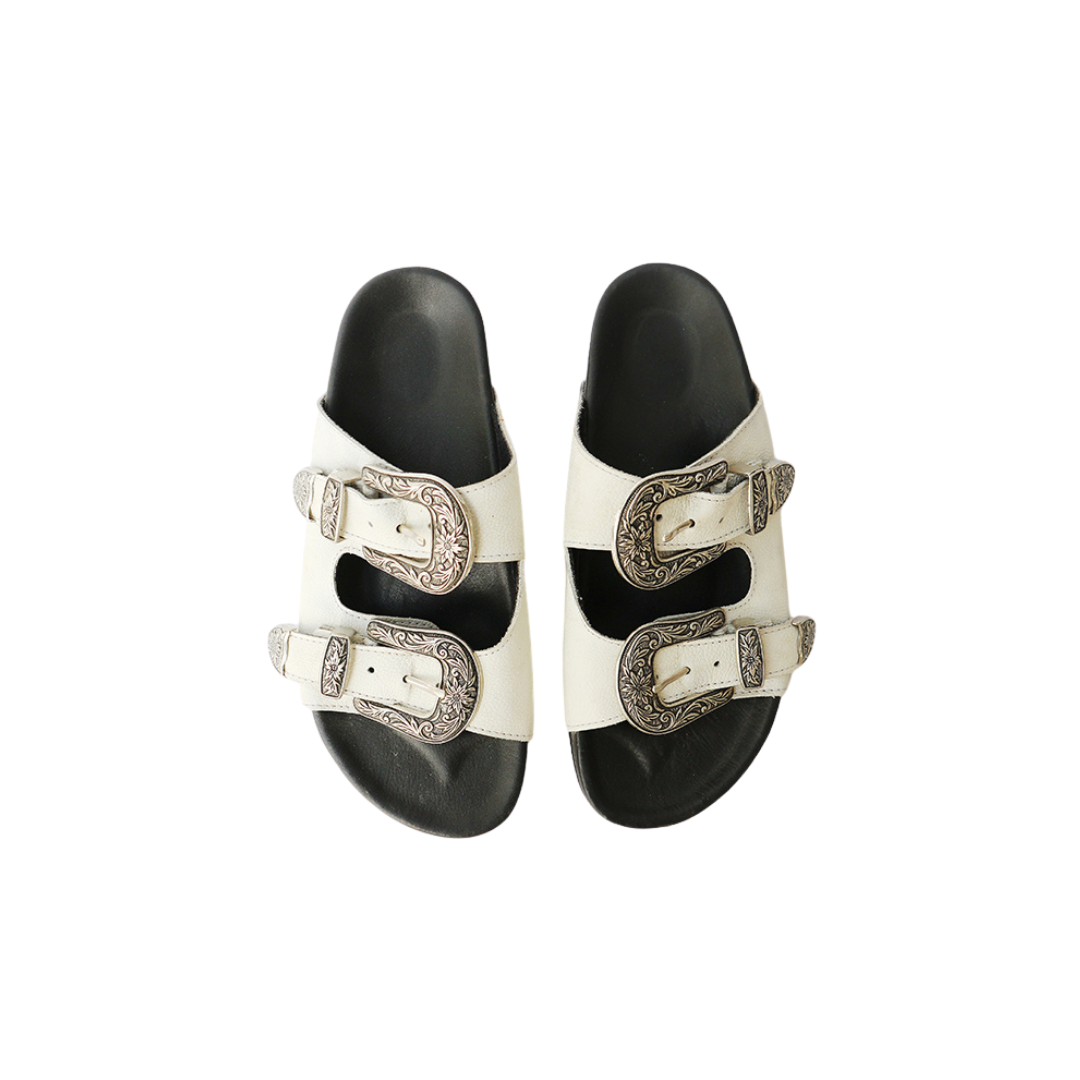 The image of a white sandal made of cowhide, designed with two straps and a carved buckle decoration is the Becky Slides Sandal from Seminyak Leather Bali