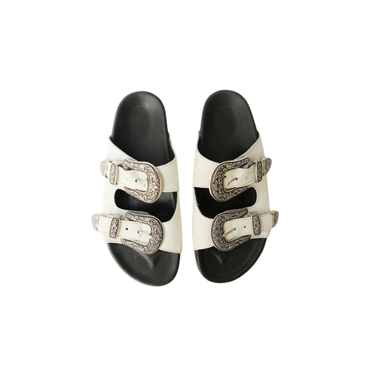 The image of a white sandal made of cowhide, designed with two straps and a carved buckle decoration is the Becky Slides Sandal from Seminyak Leather Bali