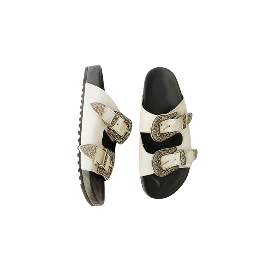 The image of a white sandal made of cowhide, designed with two straps and a carved buckle decoration is the Becky Slides Sandal from Seminyak Leather Bali
