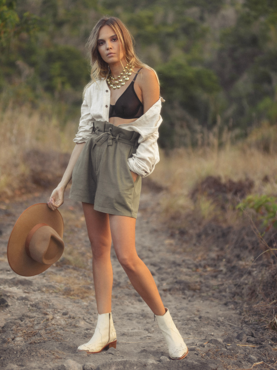 A female model stands holding a hat facing straight into the camera, wearing a cowboy suit and cream colored boots. Boots made of sheep Leather combined with carving details and 5 cm high heels are boots from the Seminyak brand Leather Bali, namely Canggu Boots.