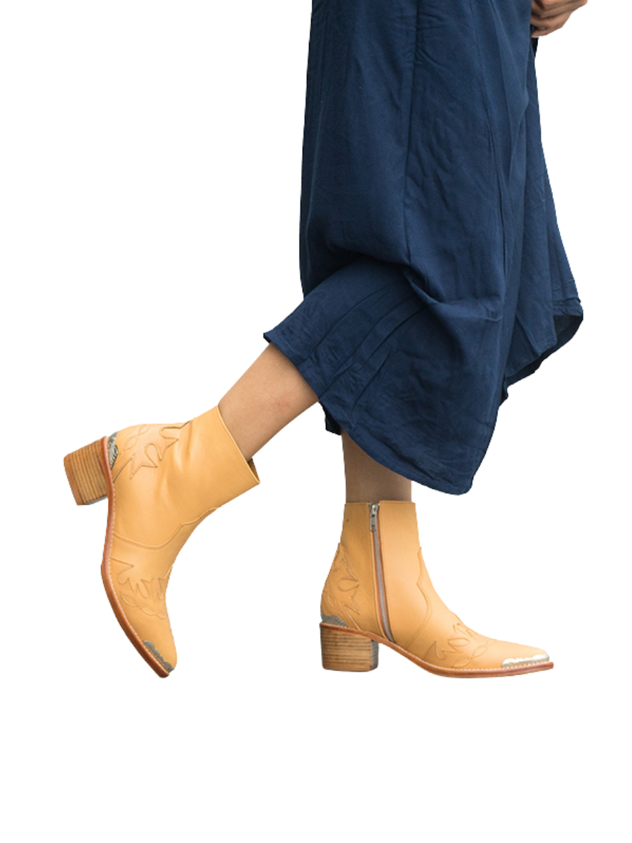 A model in a blue dress wears Tan boots with carving details around them. The boots are made of tan sheepskin with threaded carvings and additional metal carvings on the front and back as well as a ziper for ease of use and 5 cm high heels. These boots are Canggu Boots Carving from Seminyak Leather Bali