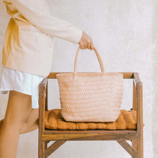 A Handwoven bag in Blush sit on the chair, holds by Model's hands. The Bag is from Seminyak Leather Bali namely Cening Bag. The Woven is handmade with our artisan.