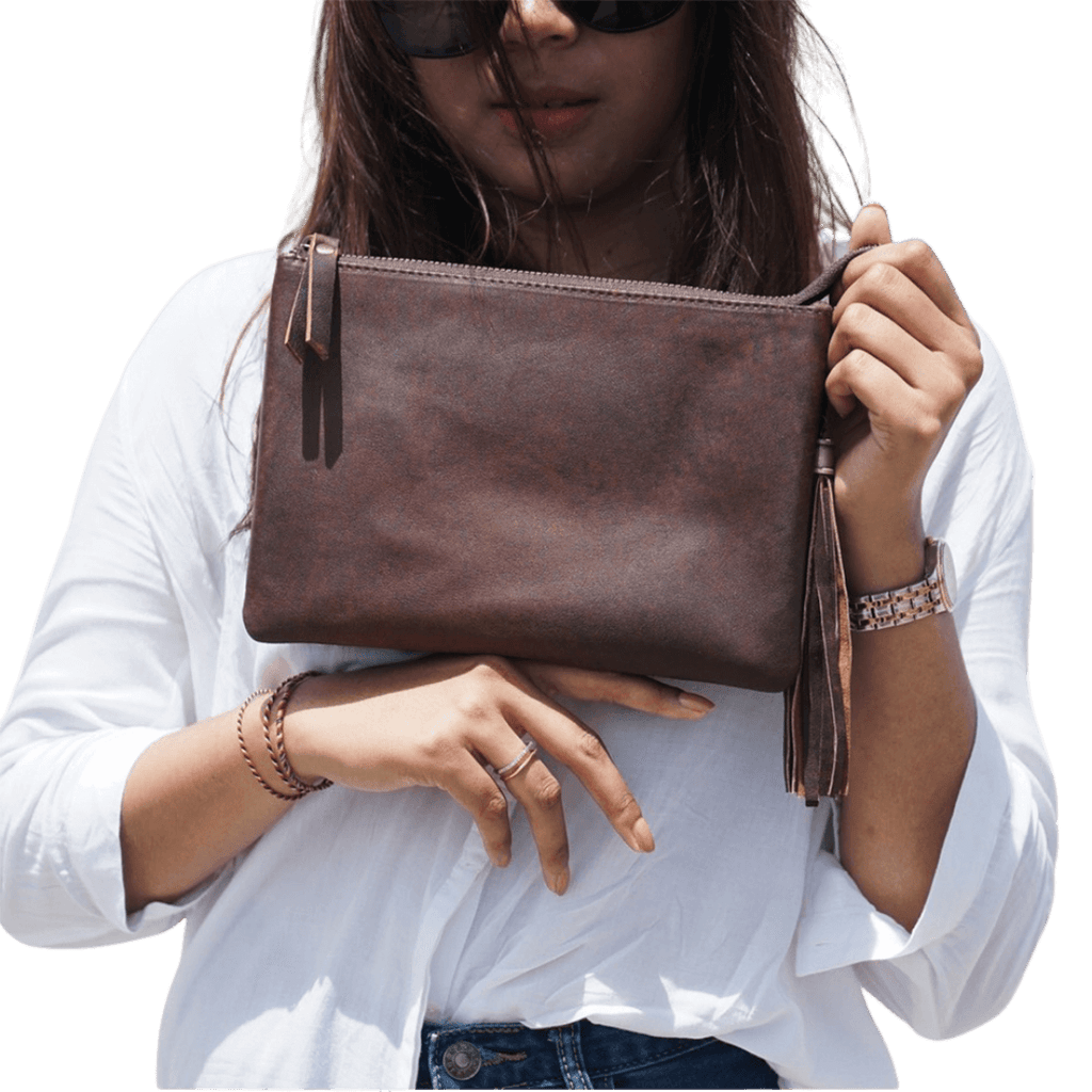 A model looking ahead, holding a clutch. Clutch made of sheep leather measuring 24 x 16 cm, antique brown color gives a unique boho impression.