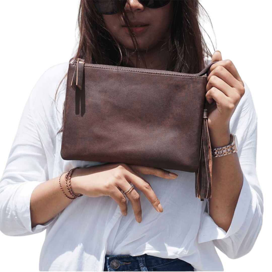 A model looking ahead, holding a clutch. Clutch made of sheep leather measuring 24 x 16 cm, antique brown color gives a unique boho impression.
