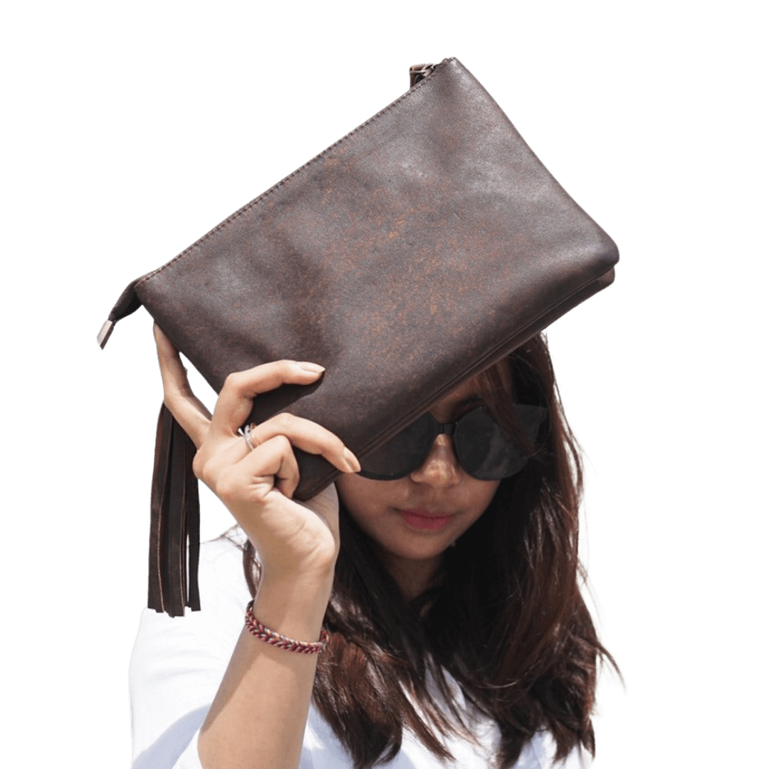 A woman model holding a 2 in 1 sheep leather clutch in Antique Brown. Look stylist with a detachable tassel and detachable strap. 