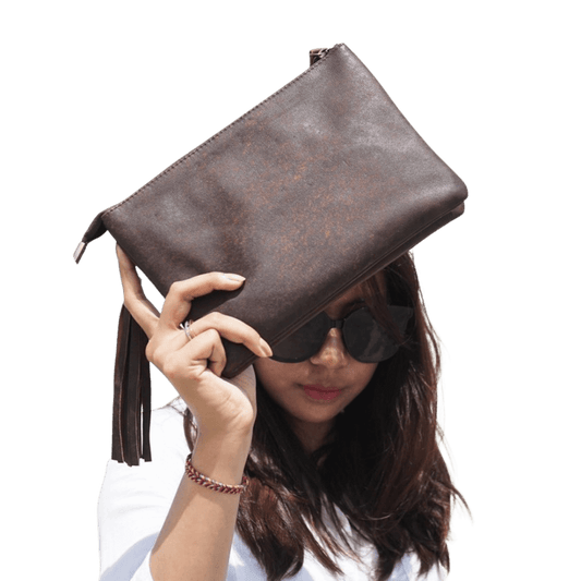A woman model holding a 2 in 1 sheep leather clutch in Antique Brown. Look stylist with a detachable tassel and detachable strap. 