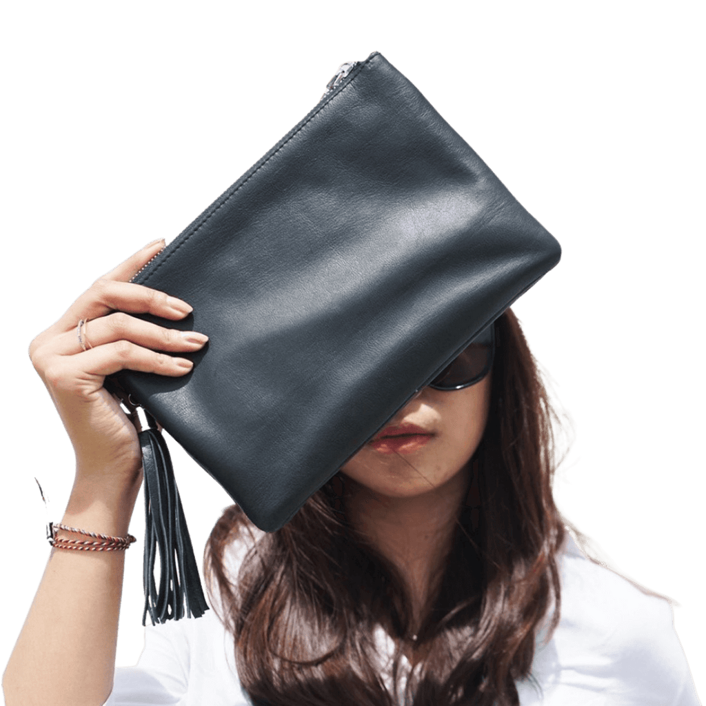 A model looking ahead, holding a clutch. Clutch made of sheep leather measuring 24 x 16 cm. The black color give you a style to make it formal or informal style. 