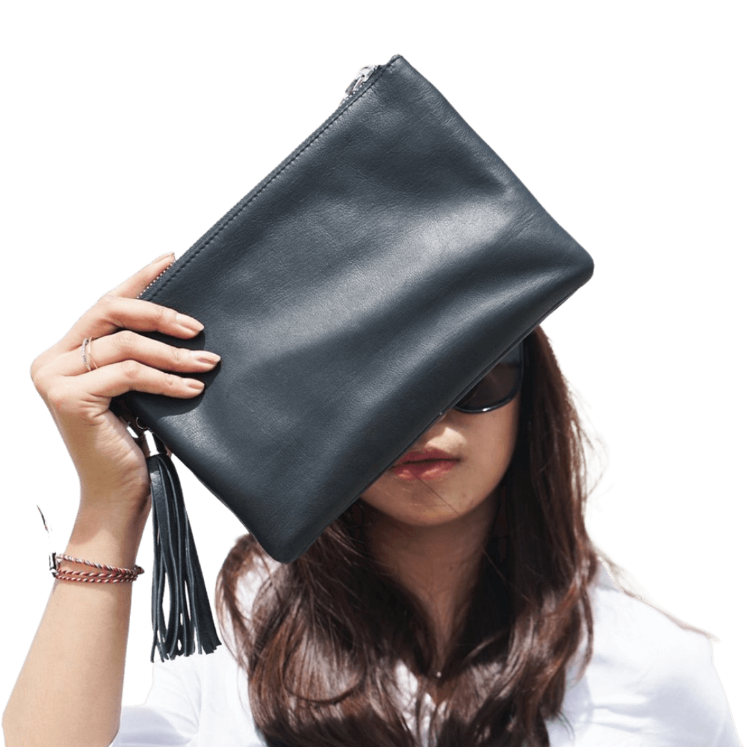 A model looking ahead, holding a clutch. Clutch made of sheep leather measuring 24 x 16 cm. The black color give you a style to make it formal or informal style. 
