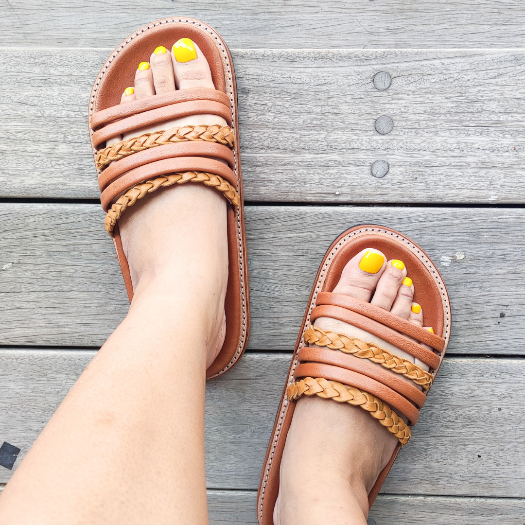 A Model shows her foot using a Sandal which have a color combination of summer tan and honey tan. The braid detail on the strap doesn't make the sandals look boring. These are Dayana Slides from Seminyak Leather Bali.
