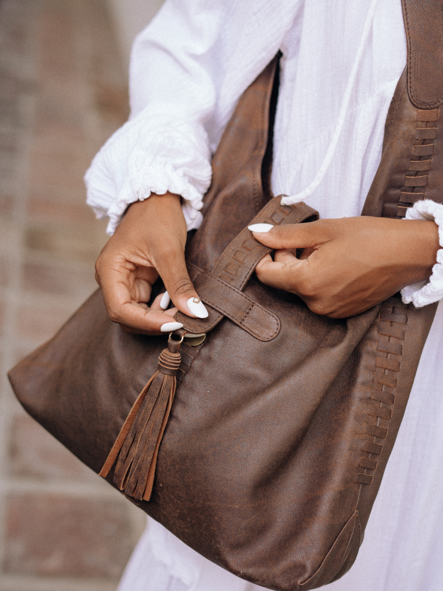 A picture showing the detail of Ella Hobo Bag, how it close fitly with the tassel and magnet closure. The hand's model shows how to close and the detail of the handwoven detail. It is Ella Hobo bag from Seminyak Leather Bali. 